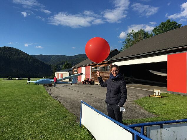 Studentin mit rotem heliumgefüllten Ballon auf dem Flugplatz